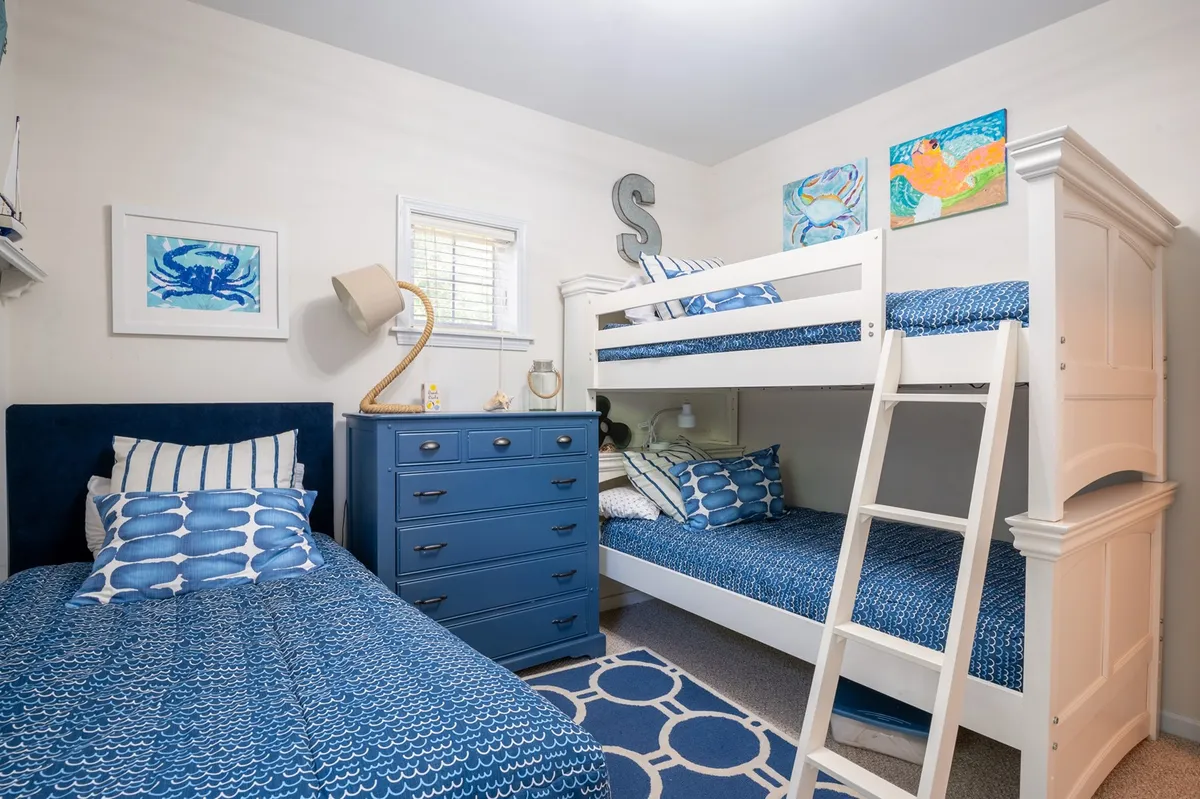 A playful and comfortable bedroom with bunk beds, a blue dresser, and cheerful artwork on the wall. The space is bright and inviting—perfect for kids or guests seeking a fun, restful environment.