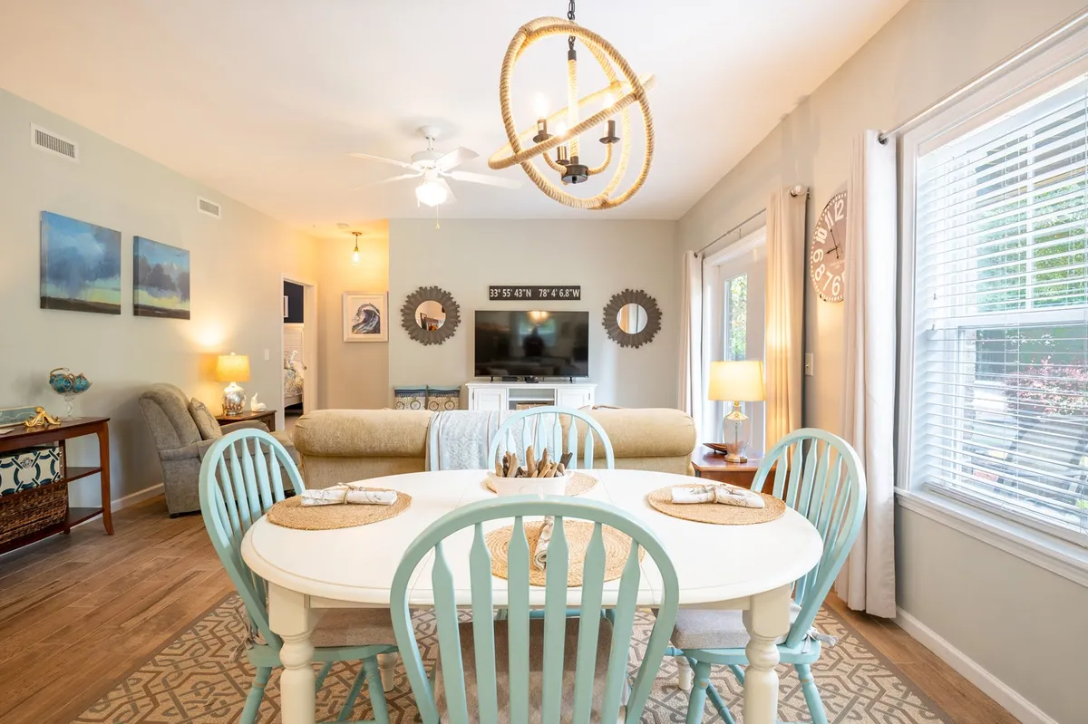 This image displays a cozy dining and living area, featuring a dining table under a chandelier, a comfortable sofa, and a TV unit. The setting feels perfect for family dinners, relaxing evenings, and shared entertainment, set against soft lighting and tasteful decor.