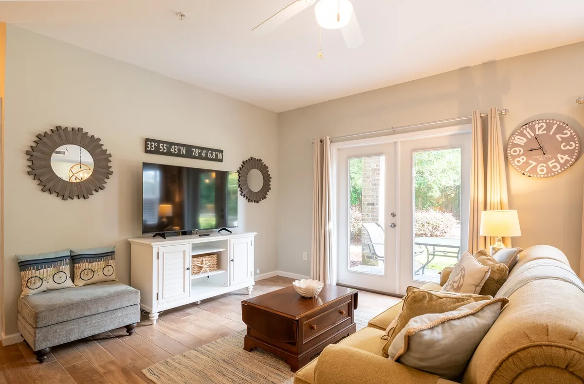 A cozy living room setup featuring a comfortable sofa, coffee table, and television. Sliding doors offer easy access to the outdoors and mirrors reflect natural light, making the space bright and inviting. The overall layout demonstrates a practical space for both everyday living and longer stays.