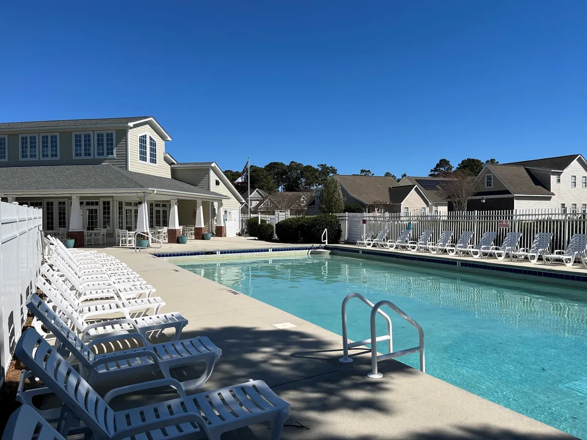 A sunlit swimming pool bordered by inviting lounge chairs and the exterior of the condo building. The pool area is designed for socializing, with ample space for groups to gather, relax, and enjoy sunny afternoons together.