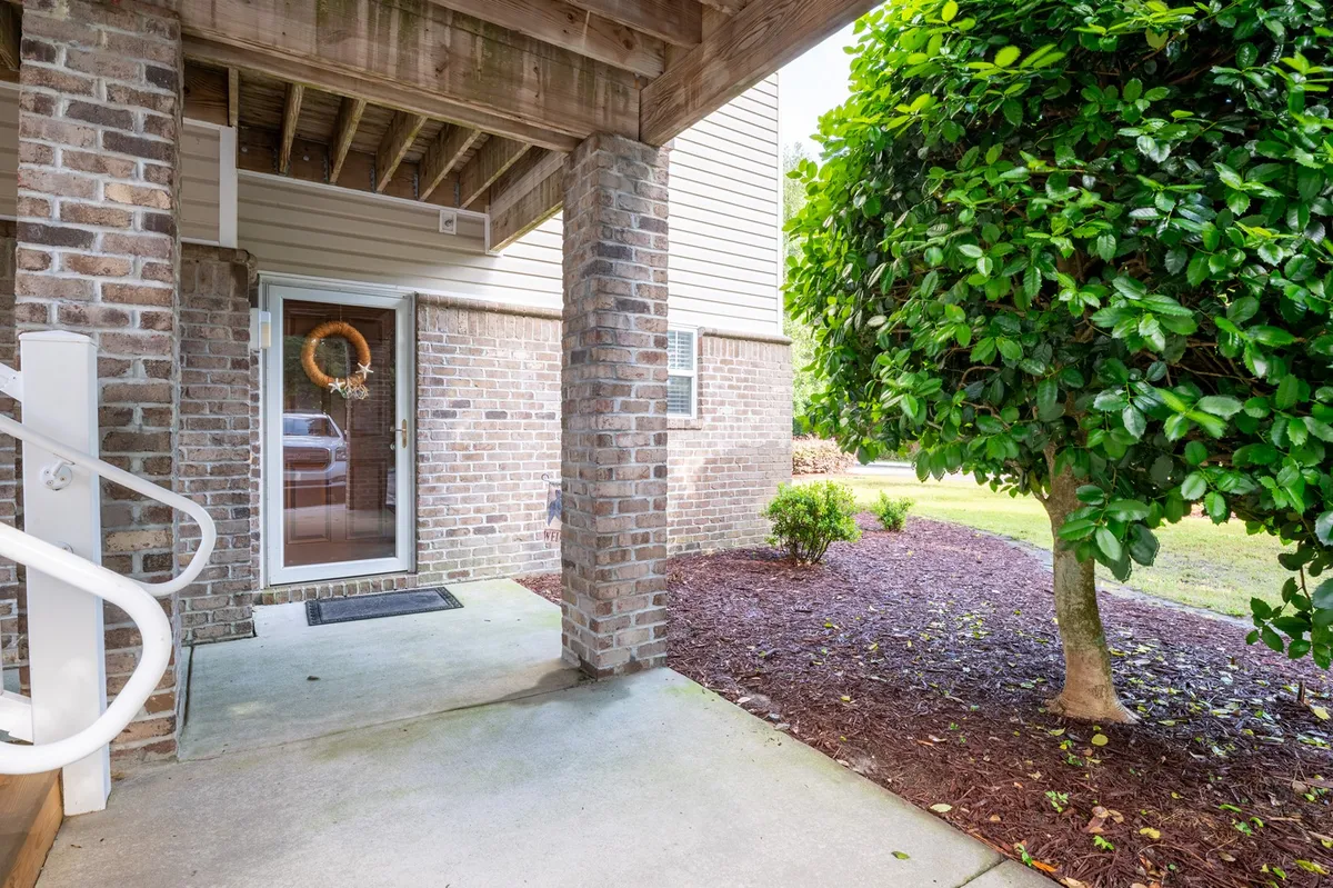 A welcoming ground-level entrance door adorned with a decorative wreath, flanked by neatly landscaped shrubs and a paved walkway. The entry is clearly accessible from street level, with no stairs in sight, emphasizing ease of access for all guests.