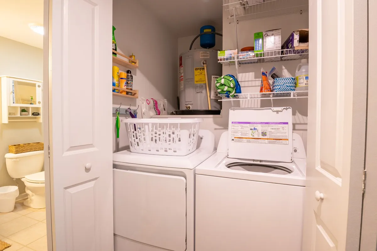 A practical laundry room with a washing machine, dryer, laundry basket, and shelves lined with cleaning supplies. The area is tidy and functional, ensuring an easy, comfortable stay for guests.