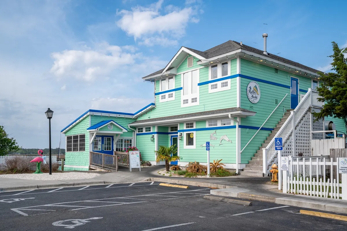 A brightly colored building with decorative signage, lush landscaping, and an adjacent parking area. The scene is vibrant and welcoming, evoking the cheerful character of Southport’s downtown area, with hints of community events and local charm.