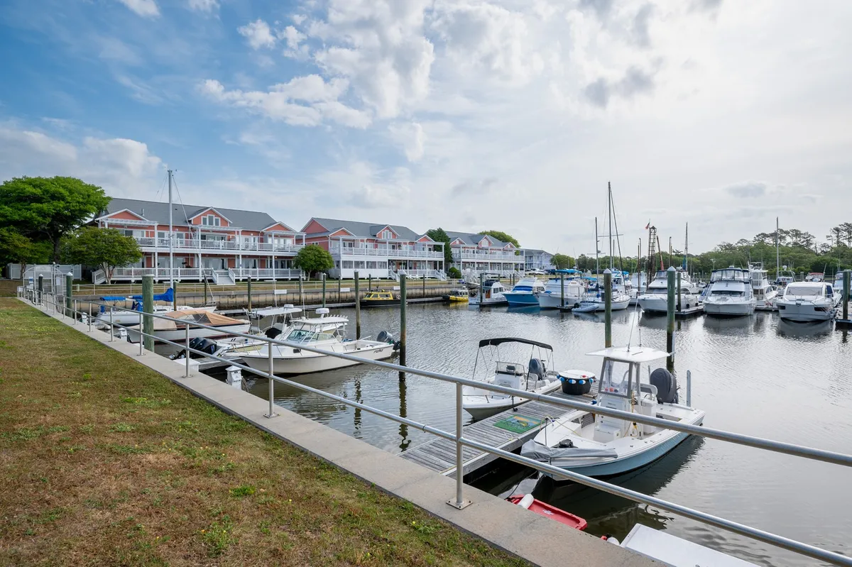 A picturesque marina scene showing boats docked along the Intracoastal Waterway, with waterfront buildings and lush green trees lining the edge. The atmosphere is peaceful, evoking relaxing strolls and waterside activities.