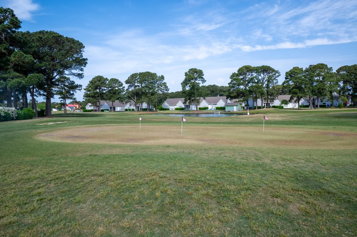 This image features a scenic golf putting green framed by residential buildings and mature trees in the background. The green and tranquil ambiance invites leisurely golf sessions and peaceful walks, visually reinforcing the section’s emphasis on golfing and relaxed outdoor activities.
