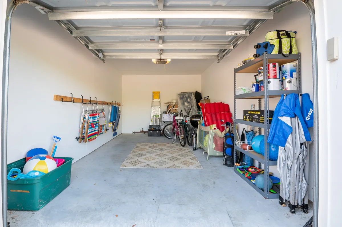 A tidy, well-lit interior garage space featuring bikes, shelves with tools and supplies, and colorful beach balls neatly stored on the floor. The atmosphere is practical yet welcoming, suggesting ample room for vacation gear.
