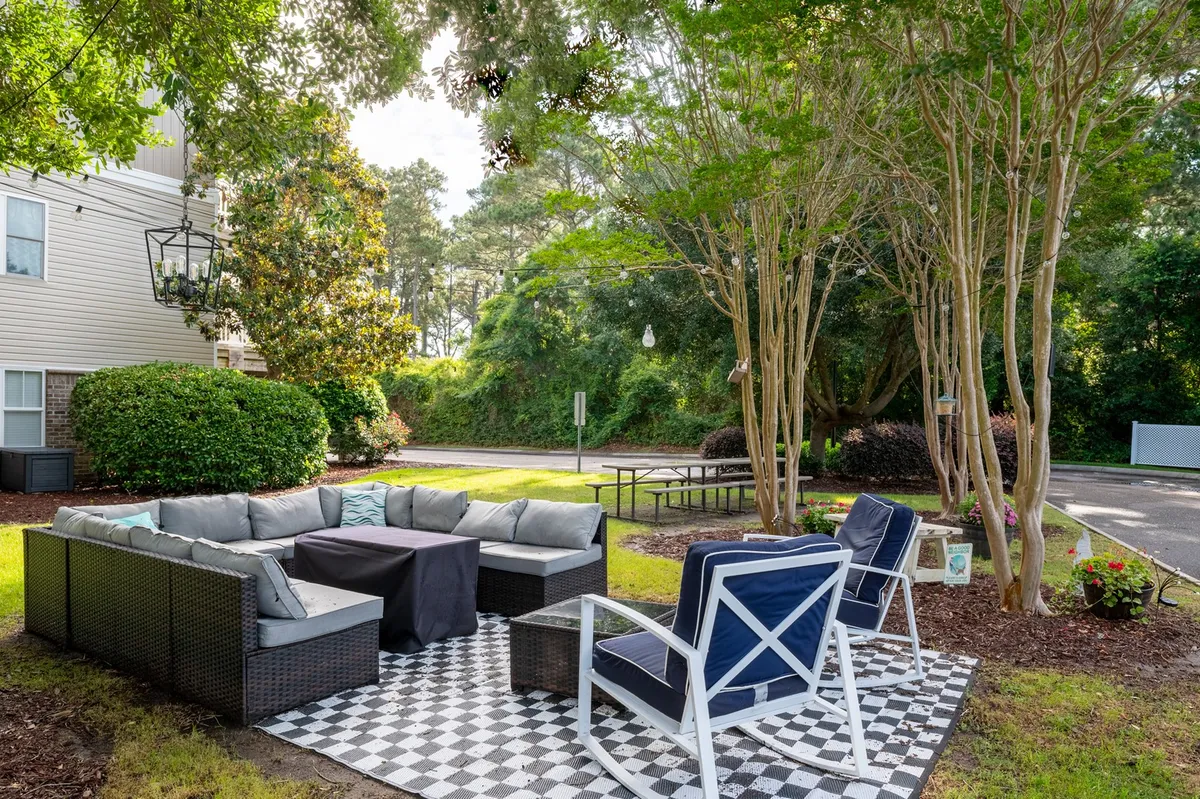 An inviting outdoor seating area with a checkerboard patio, surrounded by lush greenery and illuminated by a decorative hanging lantern. The setting is ideal for social gatherings, relaxation, and enjoying the outdoors—mirroring the lifestyle that extended stays in Southport offer.
