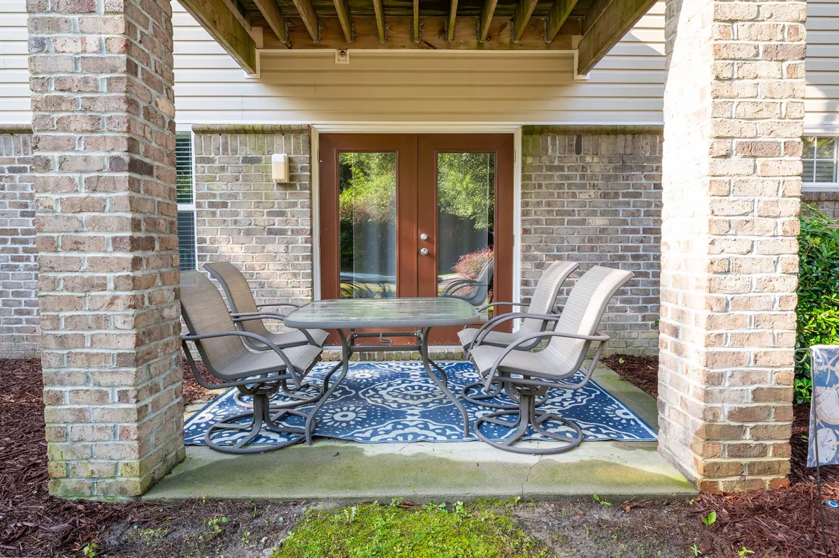 This image features a relaxed patio scene with a table and chairs set on a rug, framed by brick columns and accessed through double doors. The setting is ideal for enjoying morning coffee or sunset drinks, connecting the interior living area to the peaceful outdoors.