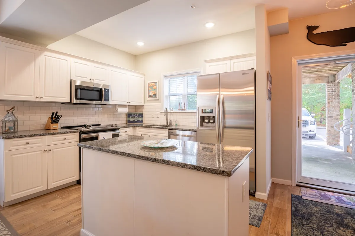 This image offers a focused view of the kitchen, featuring a spacious kitchen island topped with granite, stainless steel appliances, and a sunny window that fills the space with natural light. The warm, welcoming atmosphere invites family and friends to participate in meal preparation or casual gatherings.